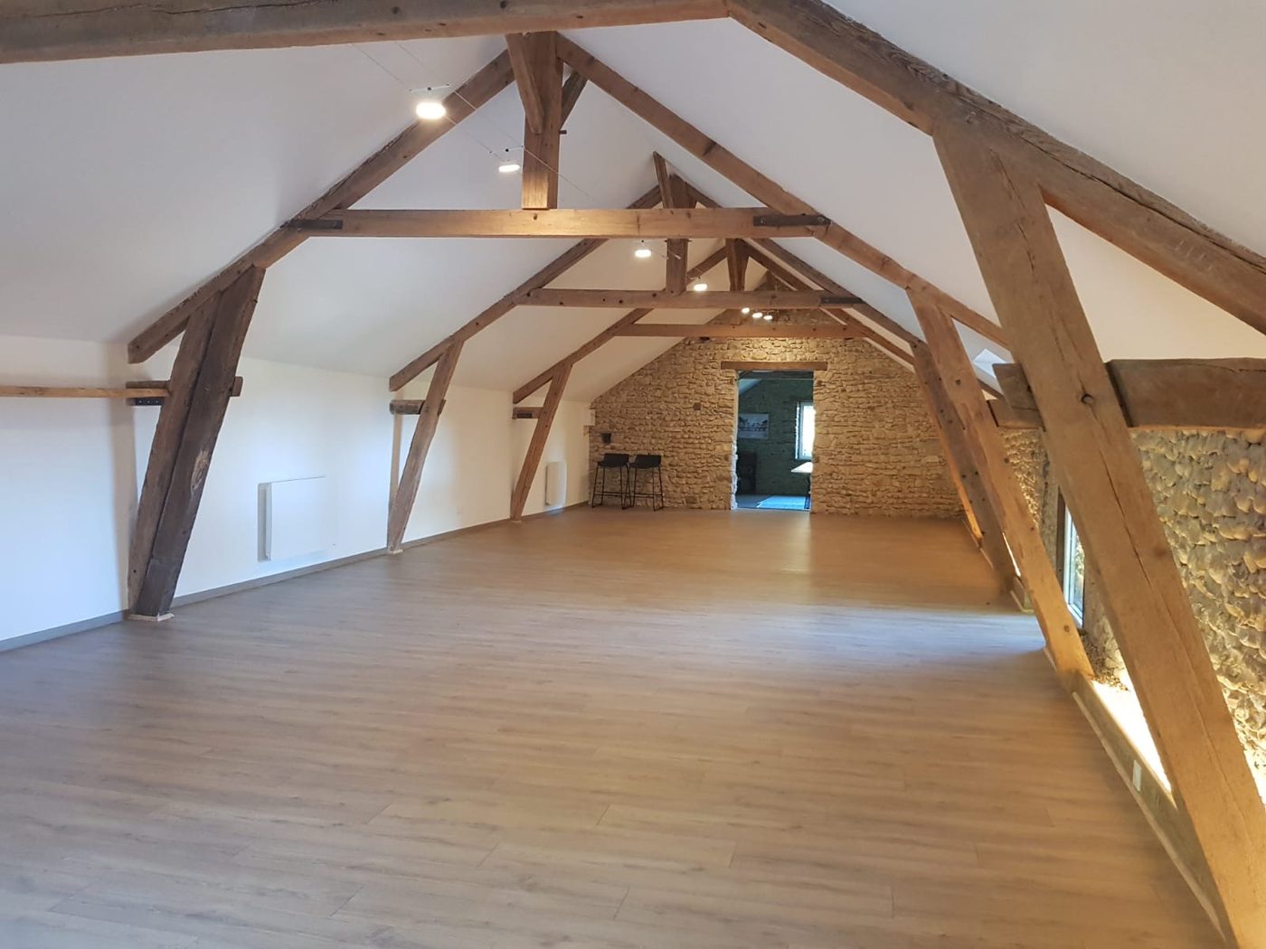 La grande salle de la Maison Amarante, sous charpente en bois apparente, avec mur en pierre